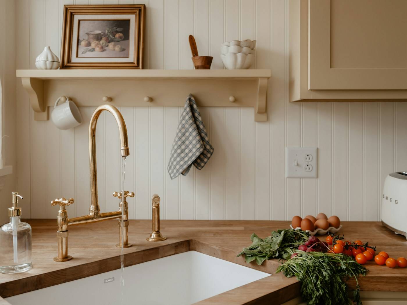 A bright kitchen sink with a wooden shelf, a glass soap dispenser and fresh vegetables on the counter