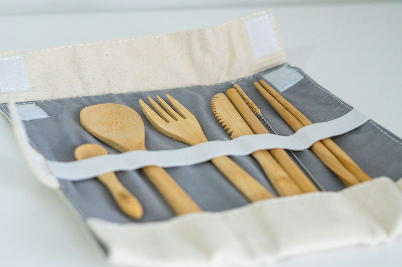 A bamboo cutlery set tucked into a grey fabric roll-up pouch