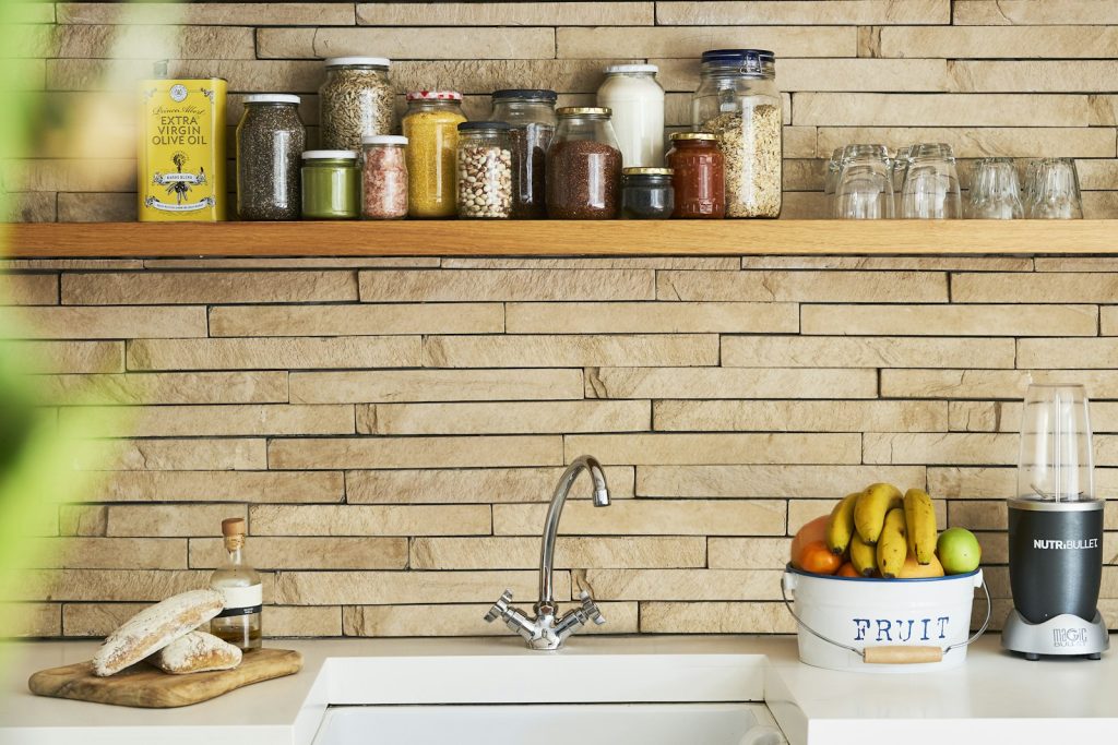 Kitchen shelf with glass storage jars above a white sink, with a bowl of bananas on the counter