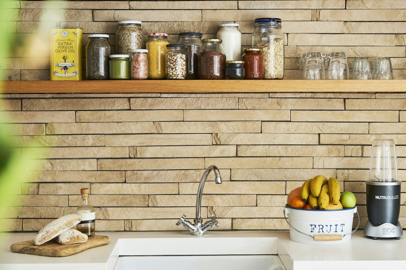 Kitchen shelf with glass storage jars above a white sink, with a bowl of bananas on the counter