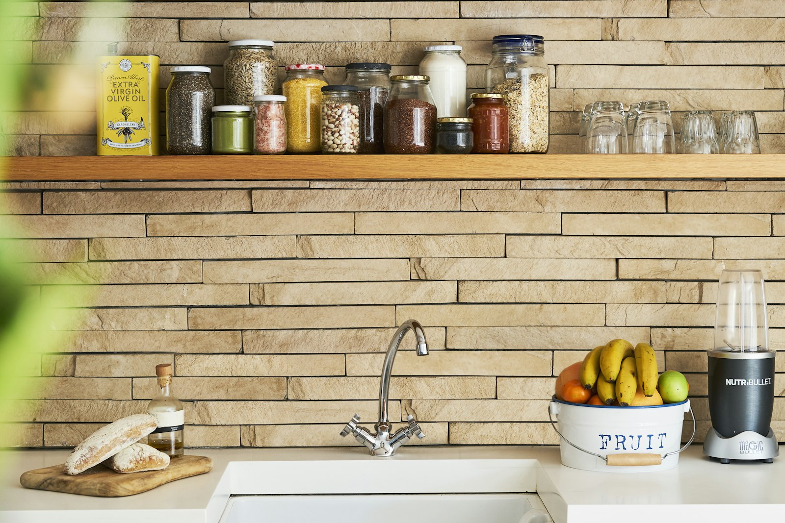 Kitchen shelf with glass storage jars above a white sink, with a bowl of bananas on the counter