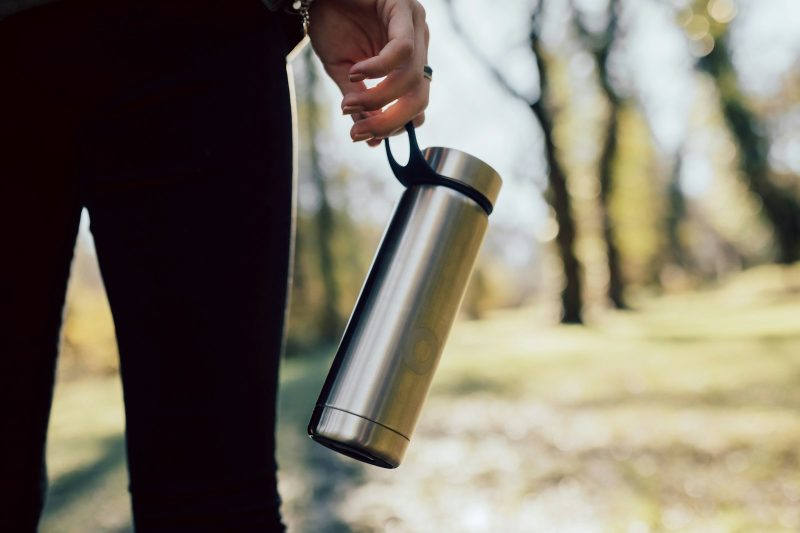A person carrying a brushed stainless steel insulated bottle by its loop outdoors