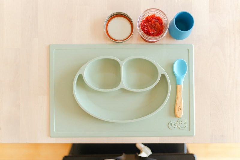 A sage green silicone suction plate for toddlers with a matching spoon and small bowls