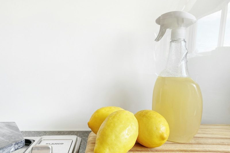 A clear spray bottle of pale yellow cleaning liquid next to fresh lemons