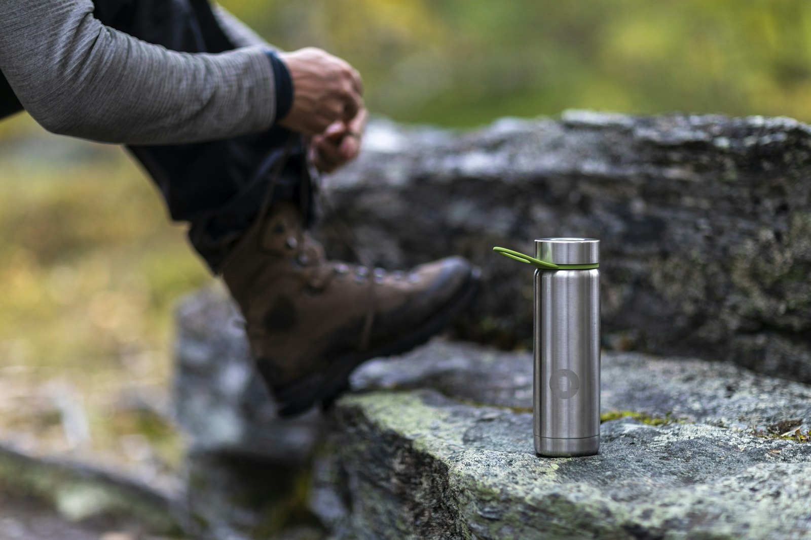 A stainless steel water bottle standing on a rock beside a hiker